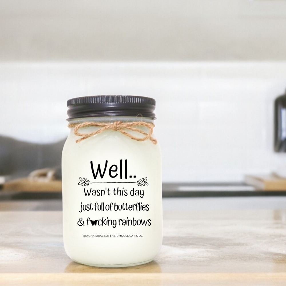 A 16 oz mason jar soy candle with a label that says "Well..Wasn't this day just full of Butterflies & F*@king Rainbows."