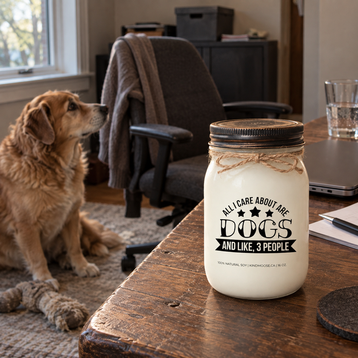 KINDMOOSE All I Care About Are Dogs and Like 3 People candle in a lived-in home office with a dog attentively watching its owner's empty desk chair.