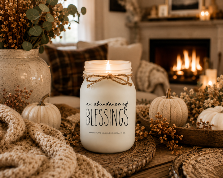 Burning AN ABUNDANCE OF BLESSINGS soy candle in an inviting autumn living room featuring a fireplace, cozy blankets, warm lighting, and a peaceful atmosphere of gratitude and comfort.