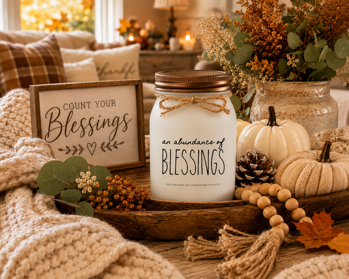 AN ABUNDANCE OF BLESSINGS soy candle with distressed bronze lid styled as a thoughtful Thanksgiving hostess gift surrounded by autumn greenery, neutral pumpkins, seasonal décor, and warm harvest accents.