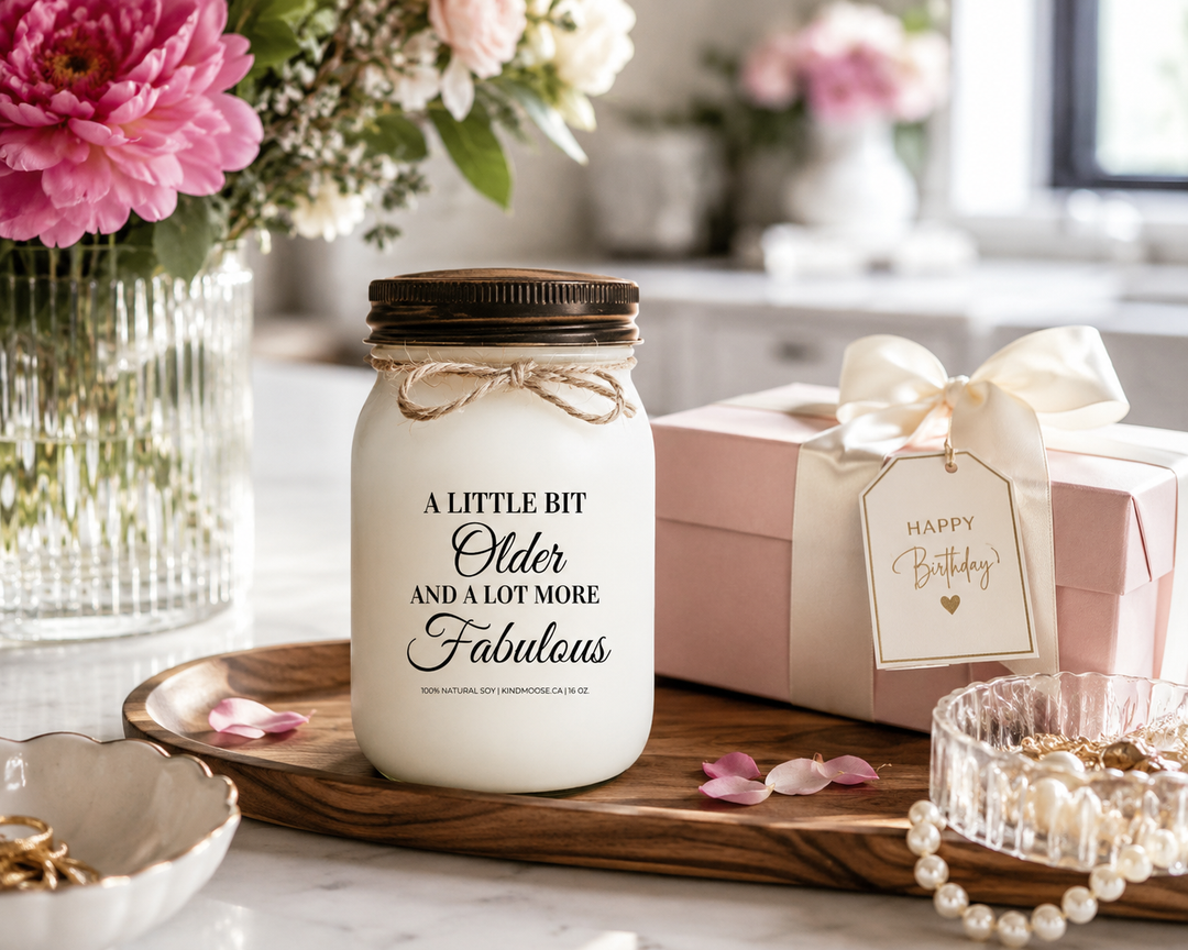 A LITTLE BIT OLDER AND A LOT MORE FABULOUS customizable soy candle with a black lid displayed on a reclaimed white oak console table in a luxury Canadian modern farmhouse. Fresh blush peonies, a gift-boxed keepsake, pinecones, and elegant birthday décor create a sophisticated birthday celebration scene filled with warmth and style.
