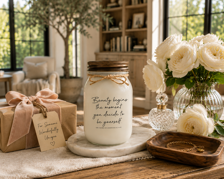 BEAUTY BEGINS THE MOMENT YOU DECIDE TO BE YOURSELF KINDMOOSE candle with a distressed bronze lid presented as an inspirational gift on a reclaimed white oak library console beside a blush velvet wrapped gift, white garden roses, crystal perfume bottle, walnut tray with a gold bracelet, and marble catchall in a luxury Canadian modern farmhouse library.