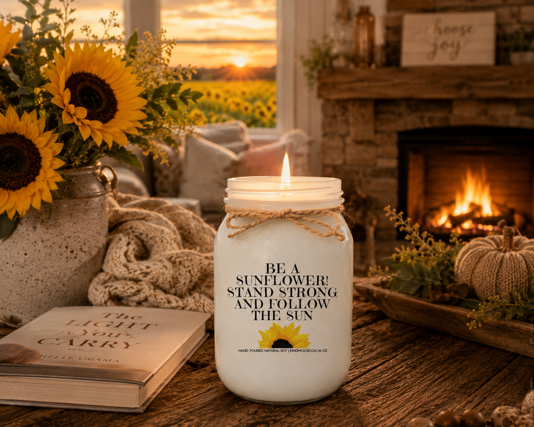 Burning BE A SUNFLOWER! STAND STRONG AND FOLLOW THE SUN soy candle in a cozy farmhouse living room featuring a stone fireplace, fresh sunflowers, soft blankets, and a warm inspirational atmosphere.