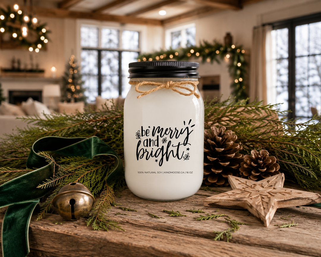 Be Merry and Bright customizable Christmas candle with a black lid displayed on a reclaimed white oak console table surrounded by fresh cedar branches, pinecones, an antique brass sleigh bell, emerald velvet ribbon, and a carved wooden star inside a luxury Canadian modern farmhouse decorated for Christmas.