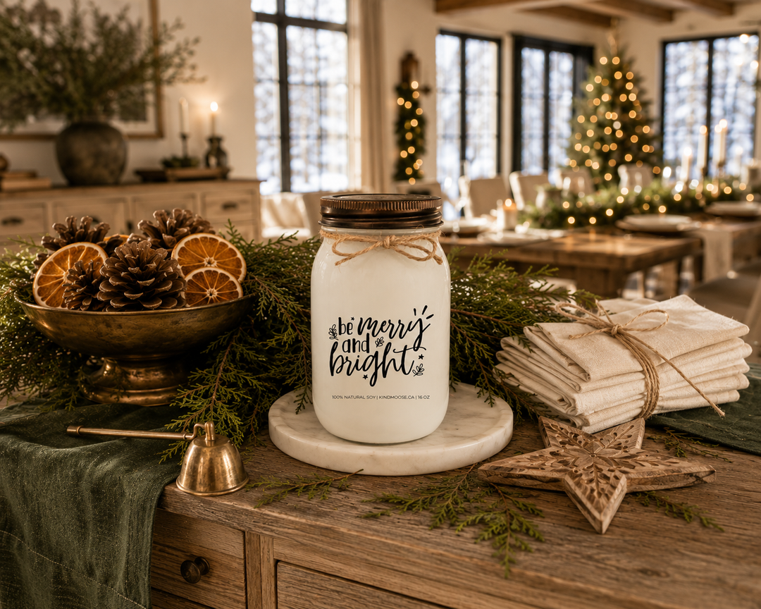 Be Merry and Bright customizable Christmas candle with a distressed bronze lid displayed on a reclaimed white oak sideboard with cedar garland, pinecones, dried oranges, ivory linen napkins, and antique brass accents in a luxury Canadian modern farmhouse dining room prepared for Christmas guests.
