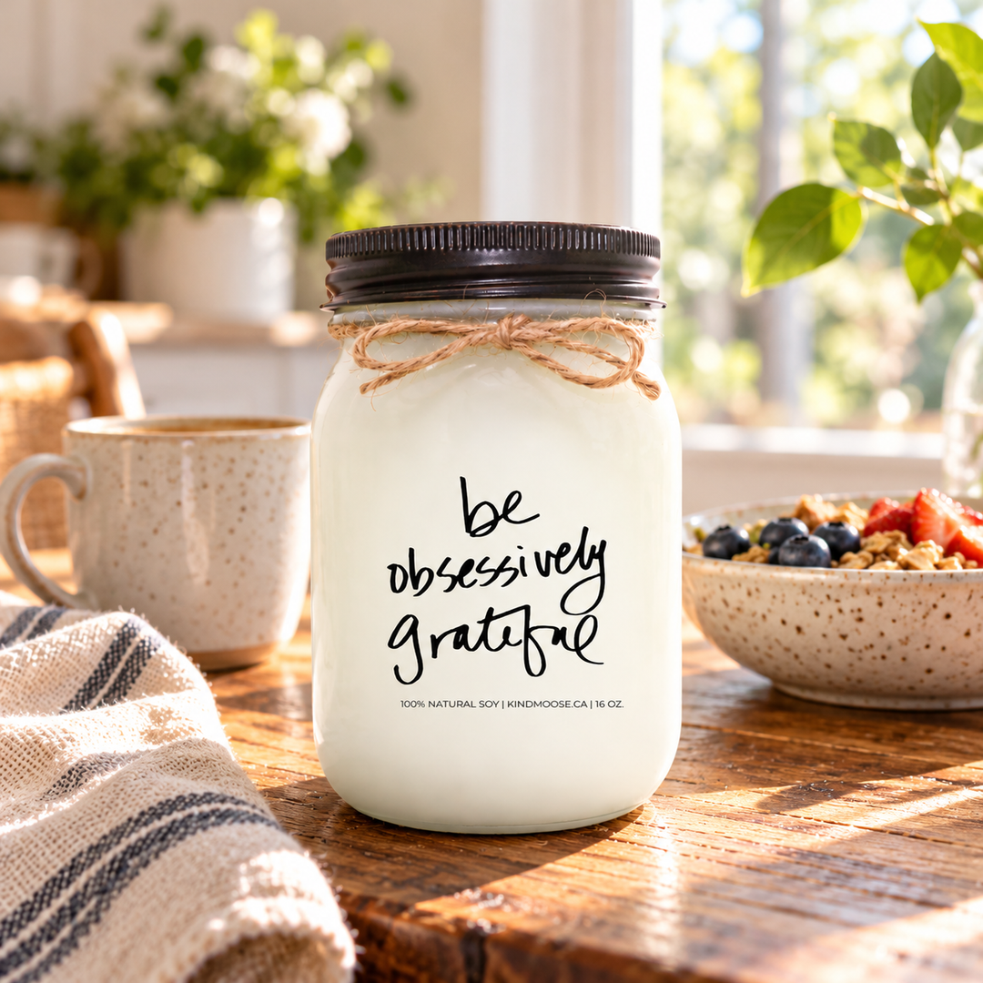 KINDMOOSE Be Obsessively Grateful 16 oz soy candle with distressed bronze lid in a welcoming kitchen, surrounded by the simple comforts of a peaceful morning.