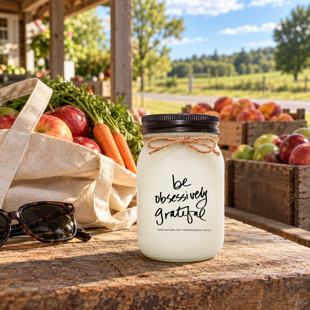 KINDMOOSE Be Obsessively Grateful candle with black lid at a countryside farm market, surrounded by fresh seasonal produce and beautiful rural Ontario scenery.