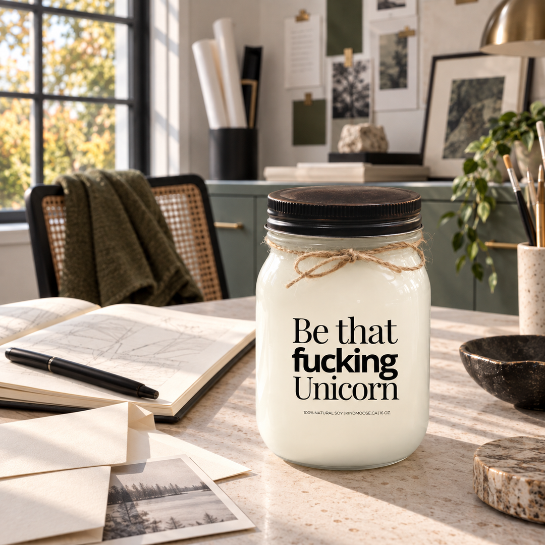 Be That Fucking Unicorn KINDMOOSE candle with distressed bronze lid in a bright creative space styled around confidence and follow-through.