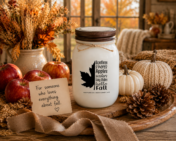 BONFIRES, S'MORES, APPLES, SWEATERS, HAY RIDES, HELLO FALL soy candle with distressed bronze lid styled as a thoughtful autumn gift surrounded by apples, pumpkins, pinecones, dried foliage, and harvest-inspired farmhouse décor.