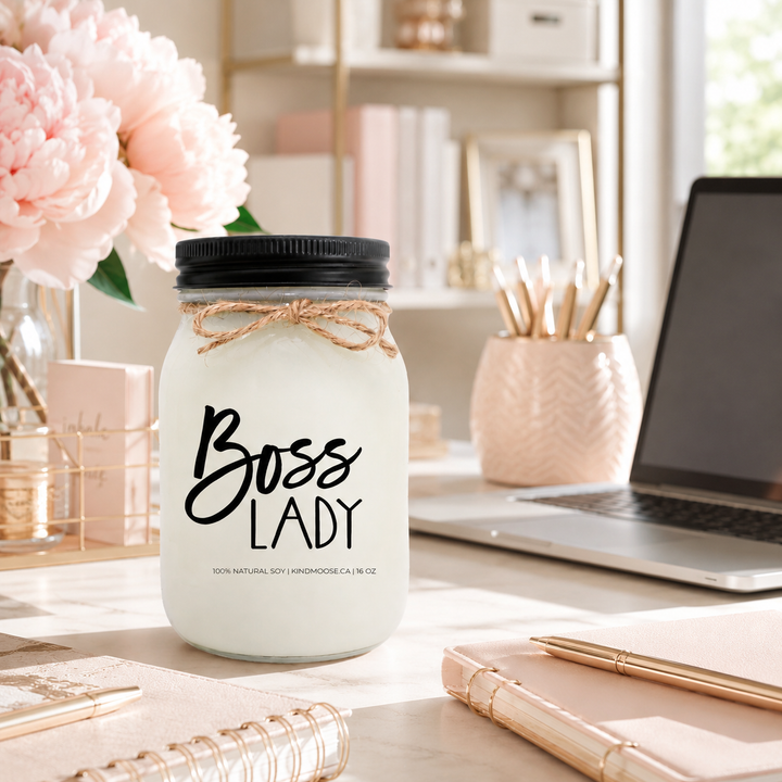 Boss Lady candle on a feminine home office desk with blush peonies, gold accents, planners and laptop in bright natural light.