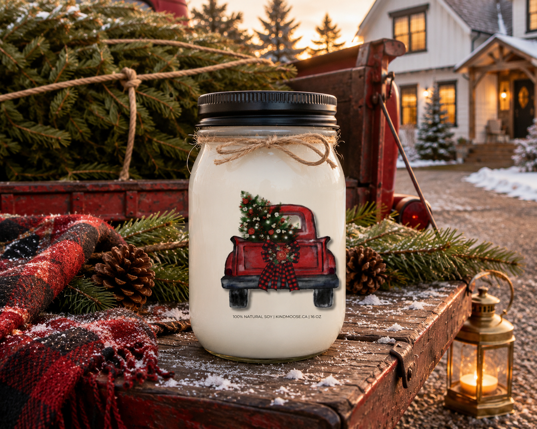 CHRISTMAS TREE TRUCK personalized Christmas candle displayed on the tailgate of a vintage red pickup truck with a freshly cut Christmas tree, cedar branches, pinecones, buffalo plaid blanket, and soft winter sunset outside a luxury modern farmhouse.