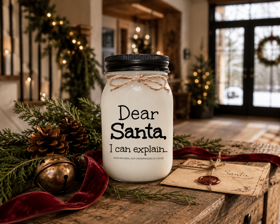 KINDMOOSE Dear Santa, I Can Explain candle with a black lid displayed on a reclaimed white oak entryway console decorated with cedar branches, pinecones, a vintage letter to Santa, cranberry velvet ribbon, and warm Christmas décor inside a luxury Canadian modern farmhouse.