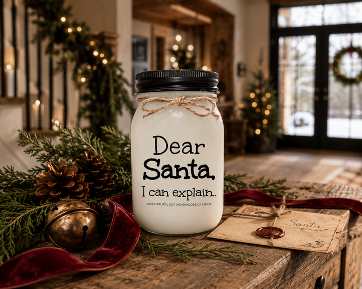 KINDMOOSE Dear Santa, I Can Explain candle with a black lid displayed on a reclaimed white oak entryway console decorated with cedar branches, pinecones, a vintage letter to Santa, cranberry velvet ribbon, and warm Christmas décor inside a luxury Canadian modern farmhouse.