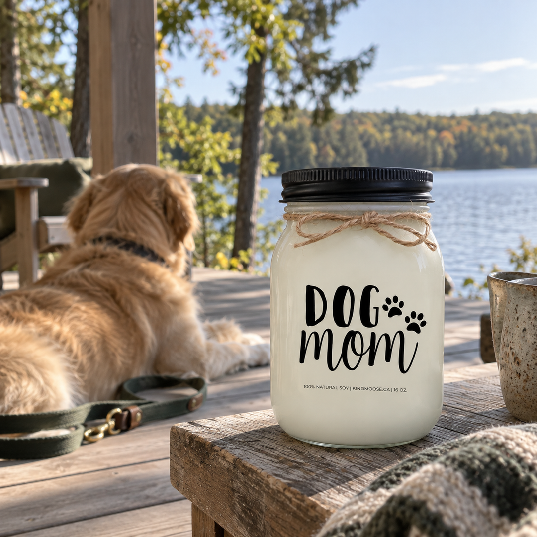 KINDMOOSE DOG MOM 16 oz candle on a lakeside cottage deck with an adult Golden Retriever nearby on a peaceful early-autumn morning.