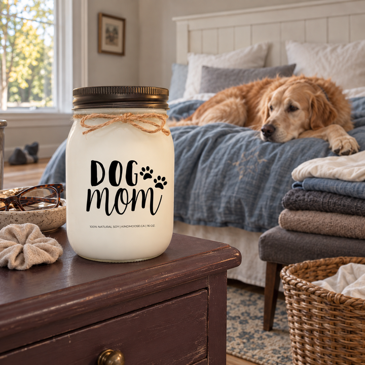 KINDMOOSE DOG MOM 16 oz candle in a cottage bedroom with a Golden Retriever relaxing on the bed beside freshly folded laundry.