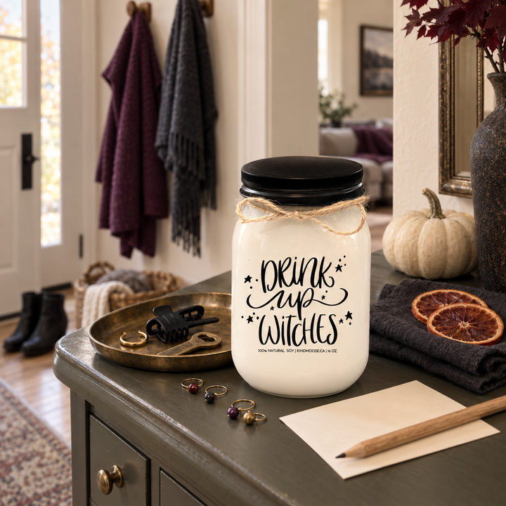 DRINK UP WITCHES KINDMOOSE candle with black lid in a quiet cottage entryway the morning after a memorable Halloween girls' night.