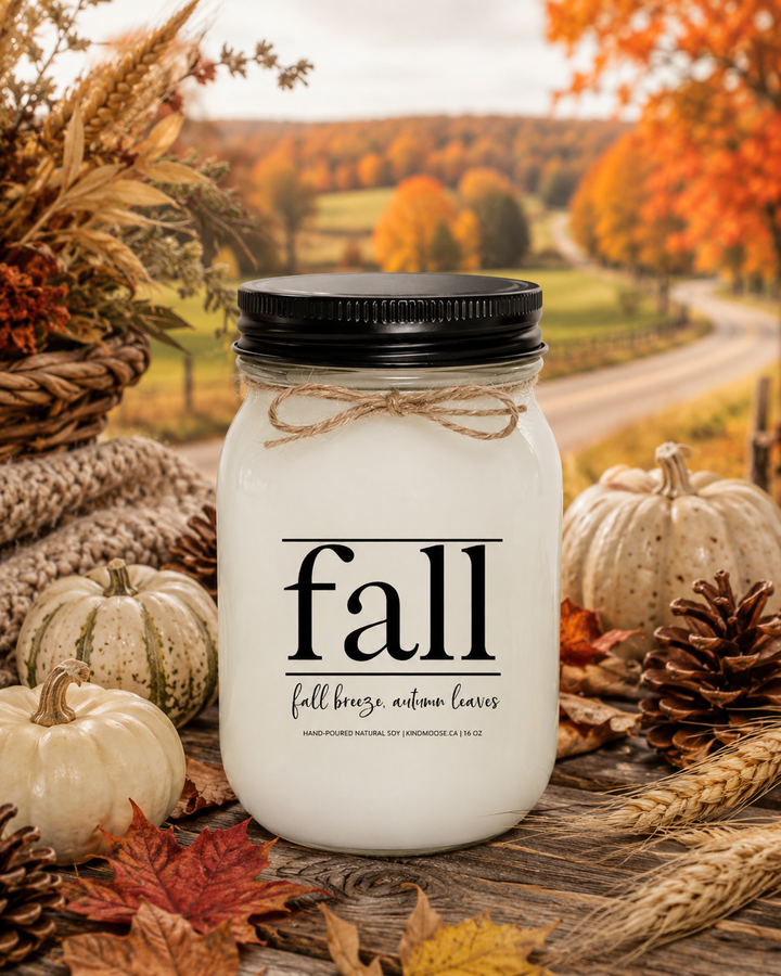 FALL | Fall Breeze, Autumn Leaves soy candle displayed on a rustic harvest table surrounded by colourful autumn leaves, pinecones, wheat stems, pumpkins, and warm countryside fall décor during peak autumn season.