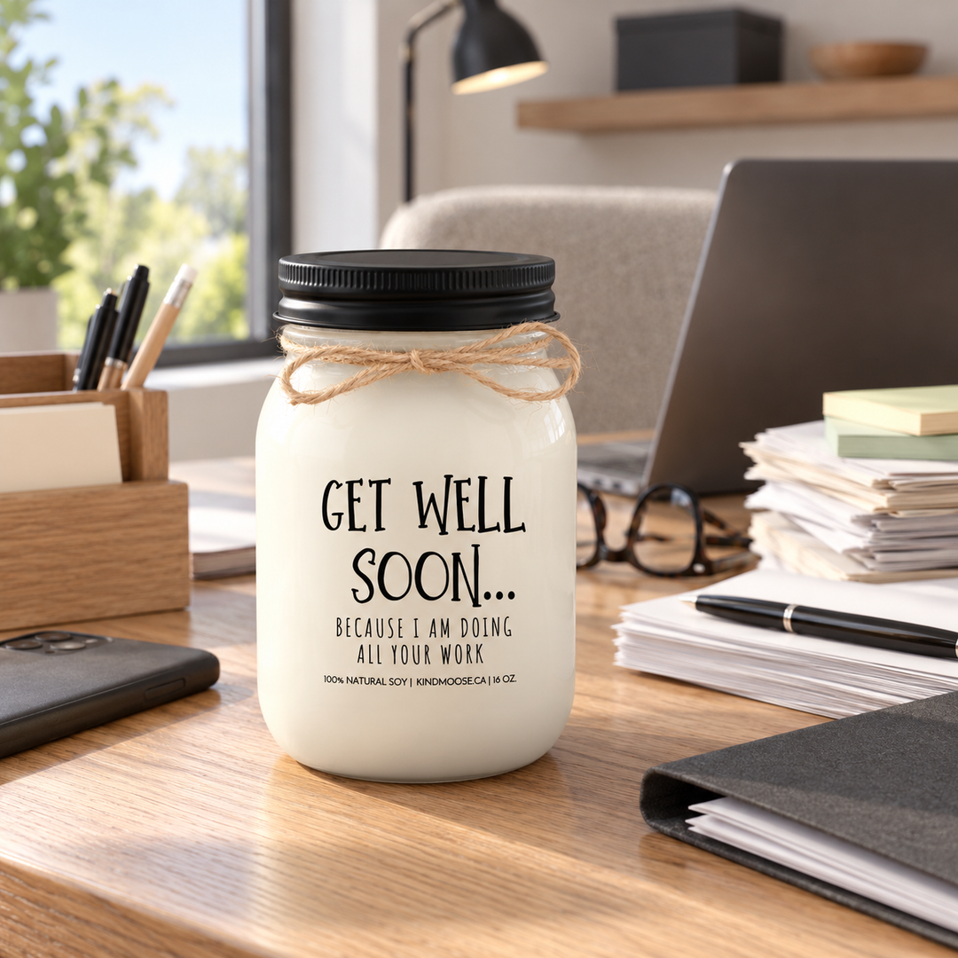 KINDMOOSE Get Well Soon Because I Am Doing All Your Work candle in a bright workspace with two workloads, a playful get well gift for coworkers.