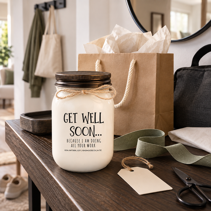 KINDMOOSE Get Well Soon Because I Am Doing All Your Work candle beside a kraft gift bag and ribbon, ready to give as a funny coworker get well gift.