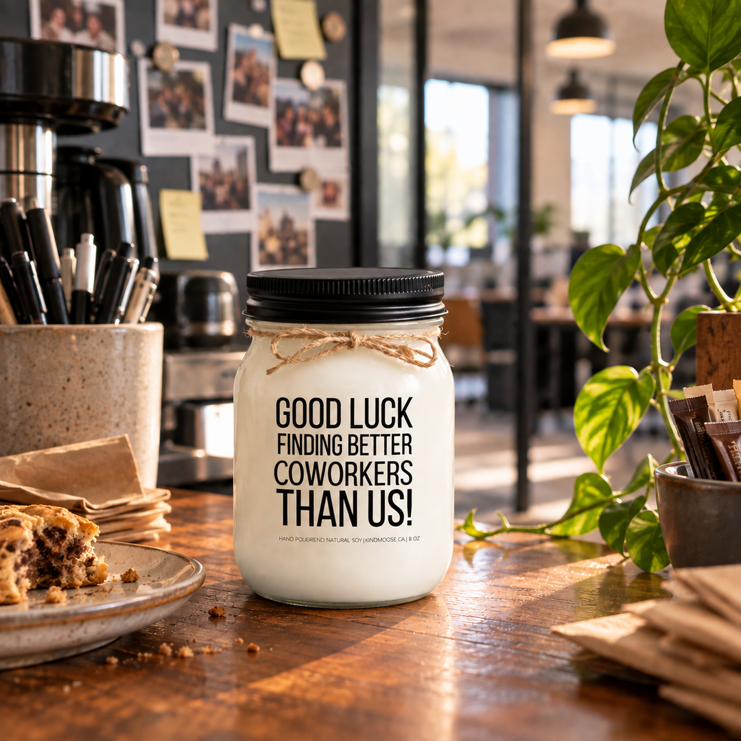 KINDMOOSE Good Luck Finding Better Coworkers Than Us candle with black lid in a casual workplace coffee area.