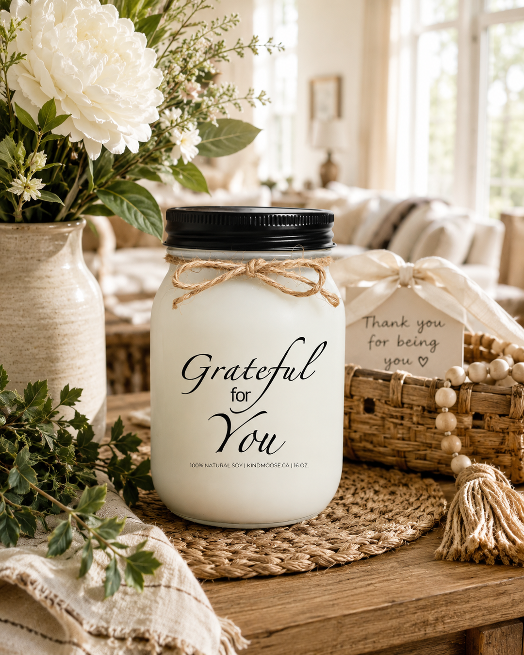 GRATEFUL FOR YOU soy candle displayed on a warm farmhouse entry table surrounded by soft white flowers, elegant greenery, woven textures, linen accents, and a neutral ceramic vase. Natural sunlight fills the bright home, creating a thoughtful atmosphere that celebrates gratitude, appreciation, and meaningful connections.