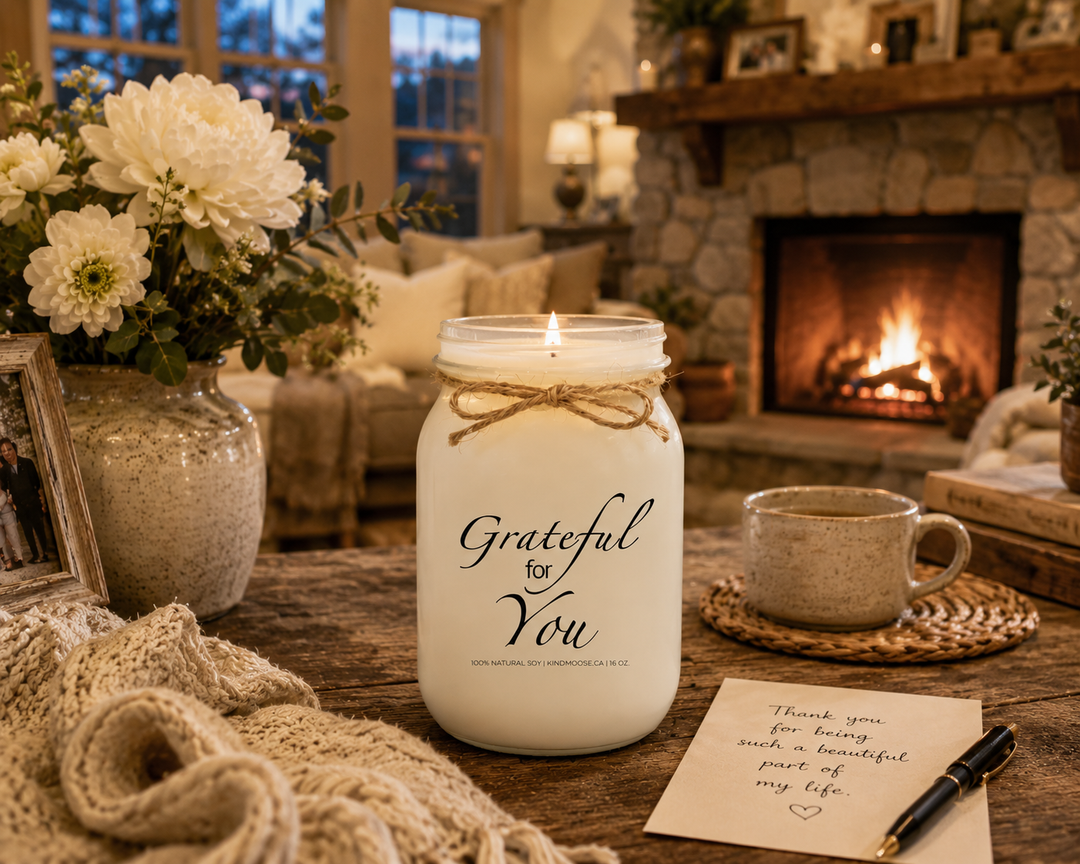Burning GRATEFUL FOR YOU soy candle in a cozy farmhouse living room featuring a stone fireplace, handwritten thank-you note, white flowers, knit blanket, family photographs, and warm neutral décor. The peaceful evening scene celebrates gratitude, heartfelt appreciation, and the people whose kindness leaves a lasting impact.