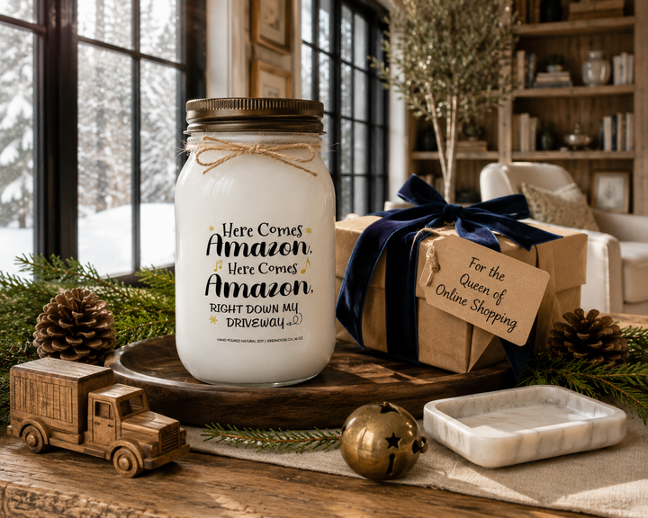 HERE COMES AMAZON, HERE COMES AMAZON, RIGHT DOWN MY DRIVEWAY candle displayed on a reclaimed white oak planning desk beside a Christmas shopping list, handwritten holiday notes, vintage stationery, cedar sprigs, and pinecones inside a peaceful Canadian farmhouse study filled with warm winter light.