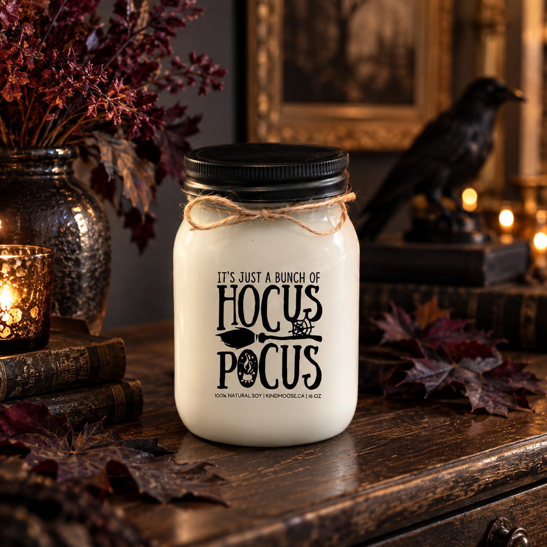 KINDMOOSE It’s Just a Bunch of Hocus Pocus 16 oz soy candle with black lid in a sophisticated Halloween setting with dark autumn foliage and a decorative raven.