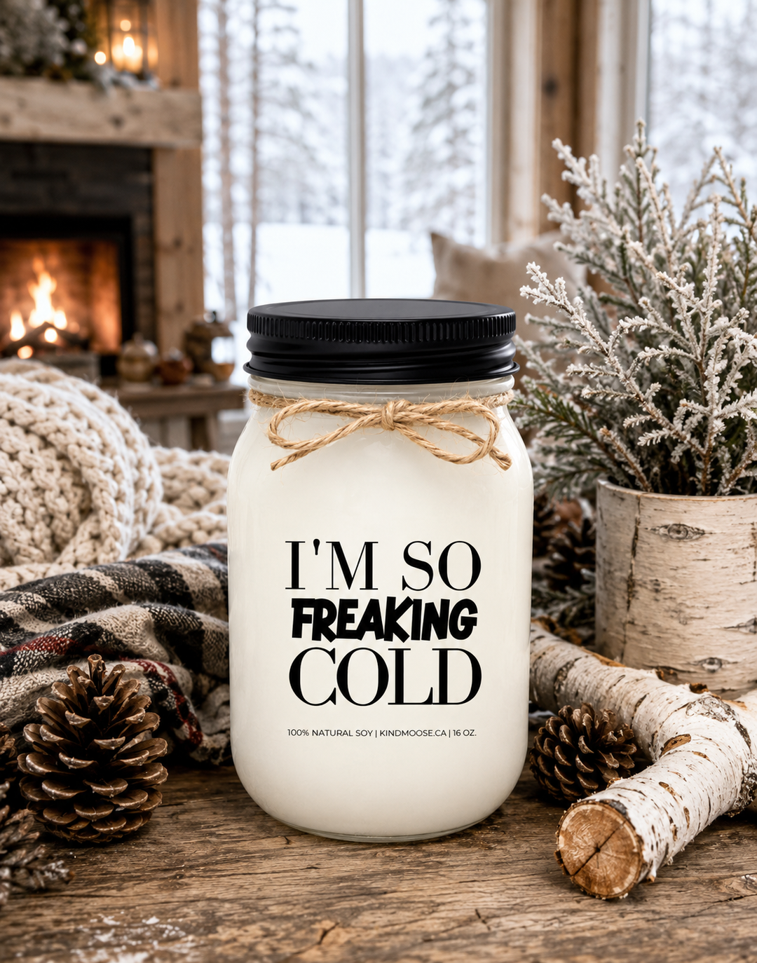 I’M SO FREAKING COLD soy candle displayed on a rustic winter farmhouse table surrounded by pinecones, white birch accents, frosted greenery, cozy knit textures, and seasonal décor. Snow-covered trees and a warm fireplace create a welcoming winter atmosphere that celebrates comfort, warmth, and surviving another cold season.