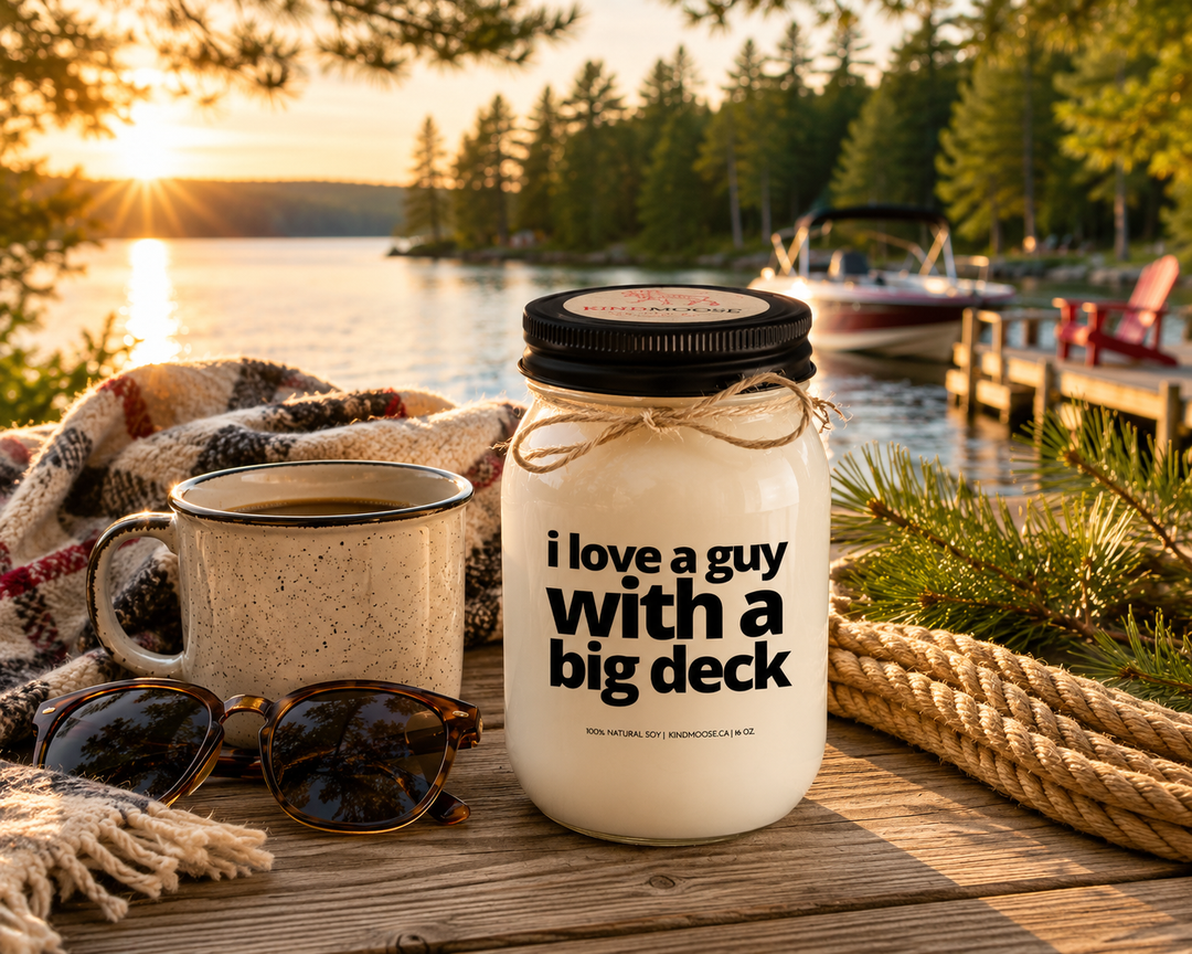 I Love A Guy With A Big Deck candle in a frosted white mason jar with black lid displayed on a rustic cottage dock overlooking a calm Canadian lake surrounded by pine trees at sunrise.