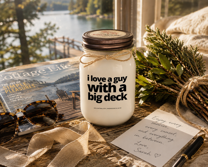 I Love A Guy With A Big Deck candle with distressed bronze lid styled as a thoughtful cottage gift beside a handwritten note, linen ribbon, greenery, sunglasses, and cottage magazine on a rustic wood table.