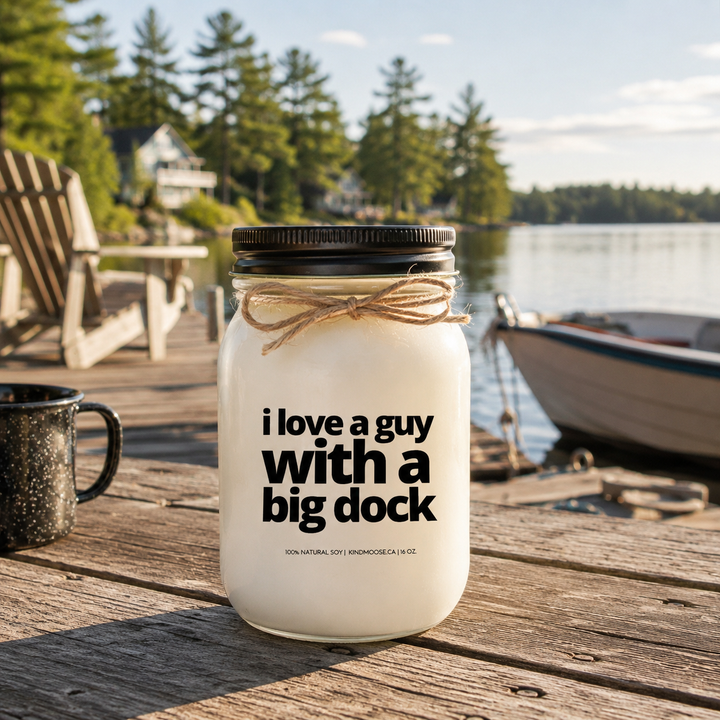 I Love A Guy With A Big Dock 16 oz soy candle on a rustic cottage dock overlooking a peaceful Canadian lake with pine trees and morning sunlight.