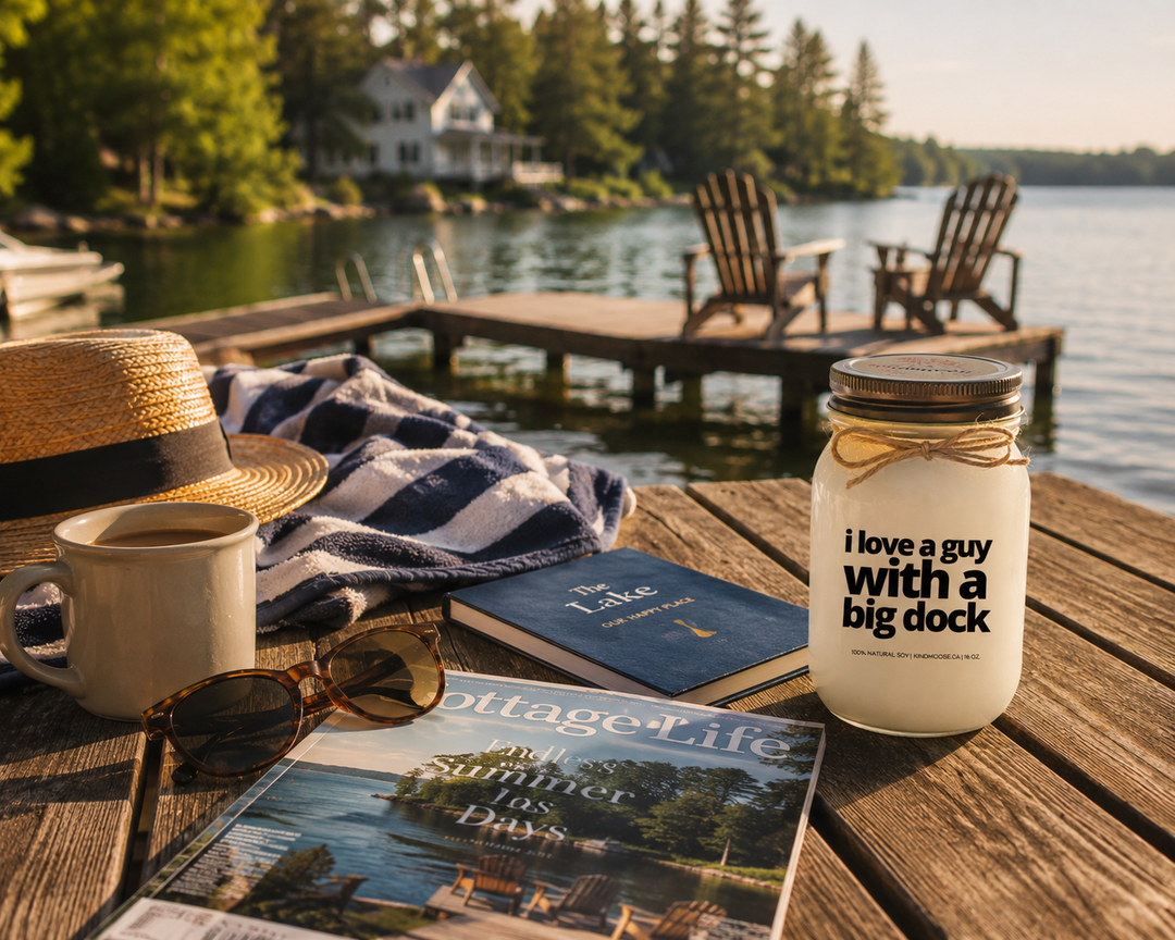 I Love A Guy With A Big Dock candle styled on a cottage dock table with coffee, sunglasses, lake magazine, cozy blanket, and waterfront view.