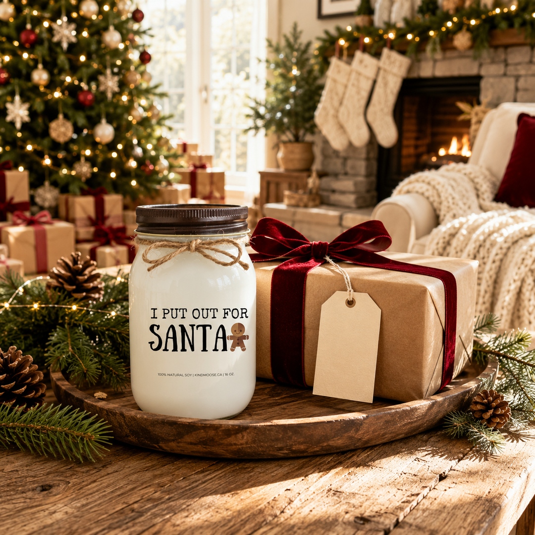KINDMOOSE "I Put Out for Santa" 16 oz frosted white soy candle presented as a funny Christmas gift beside a wrapped present with a blank gift tag in a cozy farmhouse living room decorated for Christmas morning.