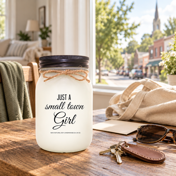 Just a Small Town Girl KINDMOOSE 16 oz candle with black lid in a bright home overlooking a familiar small Canadian town.