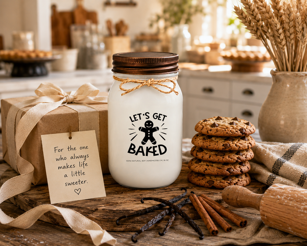 LET'S GET BAKED soy candle with distressed bronze lid displayed as a thoughtful gift on a farmhouse entry table. Surrounded by freshly baked cookies, a rolling pin, vanilla beans, cinnamon sticks, linen ribbon, wheat stems, and a handwritten gift card, the scene celebrates bakers, homemade treats, and the joy of sharing something made with love.