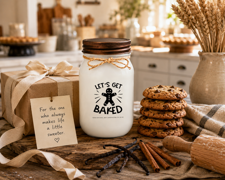 LET'S GET BAKED soy candle with distressed bronze lid displayed as a thoughtful gift on a farmhouse entry table. Surrounded by freshly baked cookies, a rolling pin, vanilla beans, cinnamon sticks, linen ribbon, wheat stems, and a handwritten gift card, the scene celebrates bakers, homemade treats, and the joy of sharing something made with love.