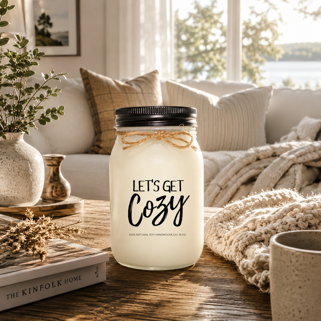 LET'S GET COZY inspirational soy candle by KINDMOOSE Candle Co. displayed on a rustic wood coffee table in a bright cottage living room with soft blankets, neutral pillows, and warm morning sunlight creating a cozy and relaxing atmosphere.