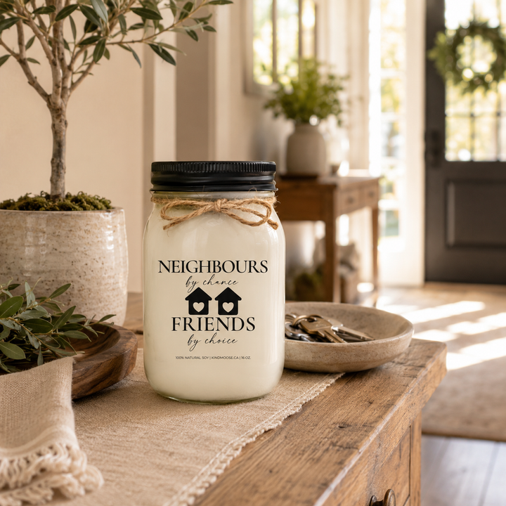 Neighbours by Chance, Friends by Choice customizable 16 oz soy candle with a black lid displayed on a reclaimed white oak entry table beside a wooden tray, ceramic key bowl, linen runner, and potted olive tree. A bright modern farmhouse entryway welcomes friends and neighbours with warm morning light.