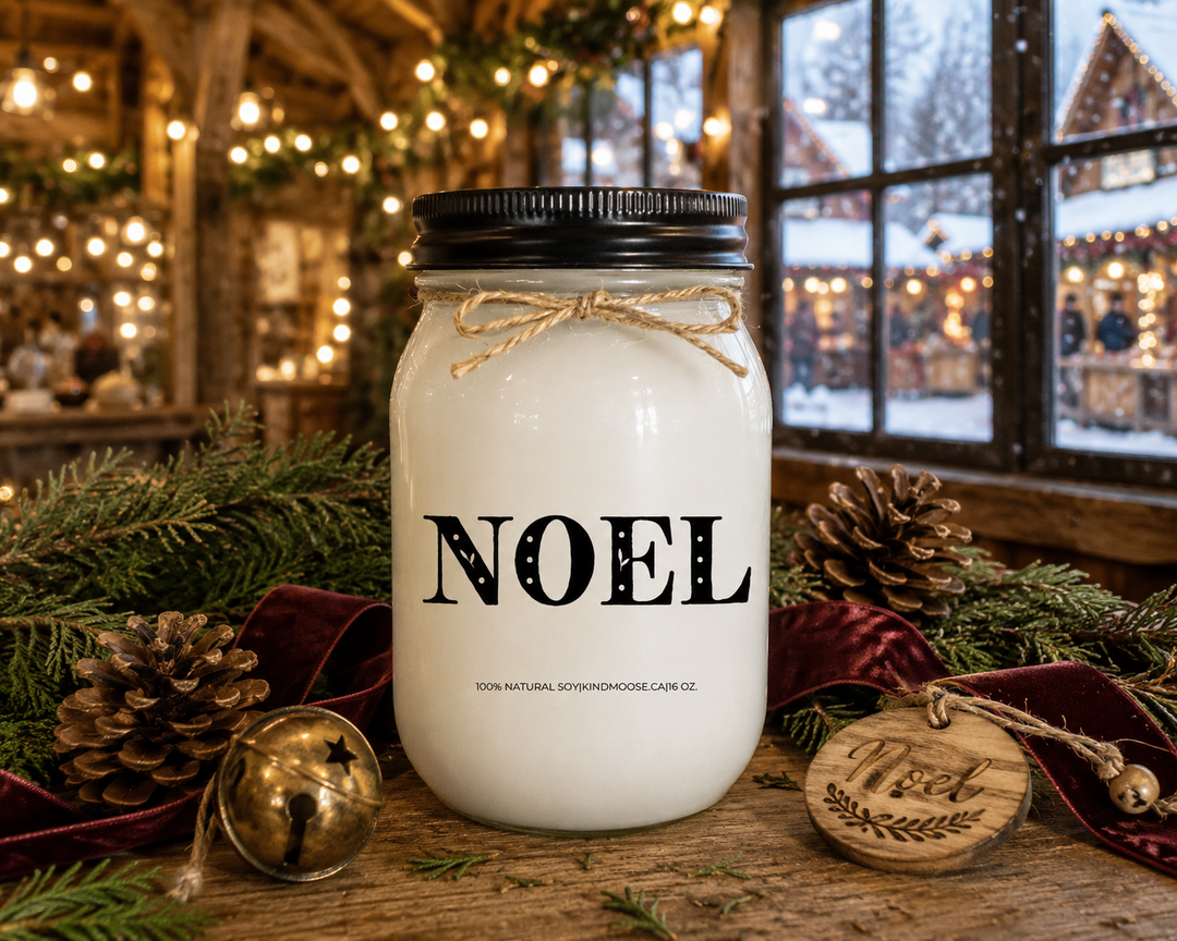 NOEL customizable Christmas candle displayed on a reclaimed white oak table inside a luxury European-style Christmas market chalet, surrounded by fresh cedar branches, pinecones, an antique brass bell, a burgundy velvet ribbon, and a handmade wooden Noel ornament, creating a timeless and elegant holiday atmosphere.