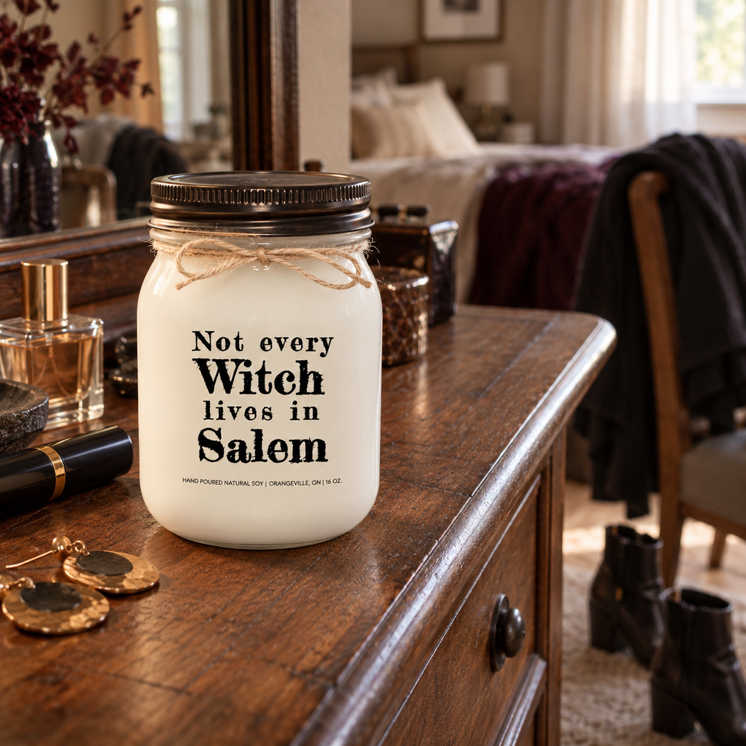 Not Every Witch Lives in Salem KINDMOOSE candle on a wood bedroom dresser with personal accessories and distressed bronze lid.