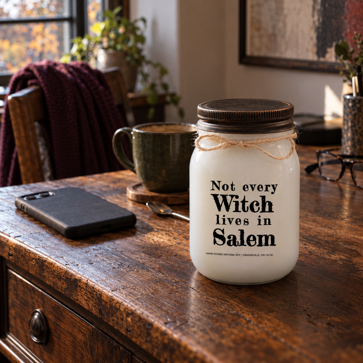 Not Every Witch Lives in Salem KINDMOOSE candle on a home office desk with a face-down phone and morning coffee.