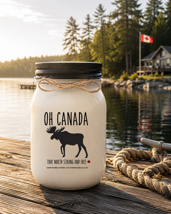 OH CANADA soy candle with black lid displayed on a rustic wooden dock overlooking a peaceful Canadian lake, surrounded by pine trees and warm morning sunlight.
