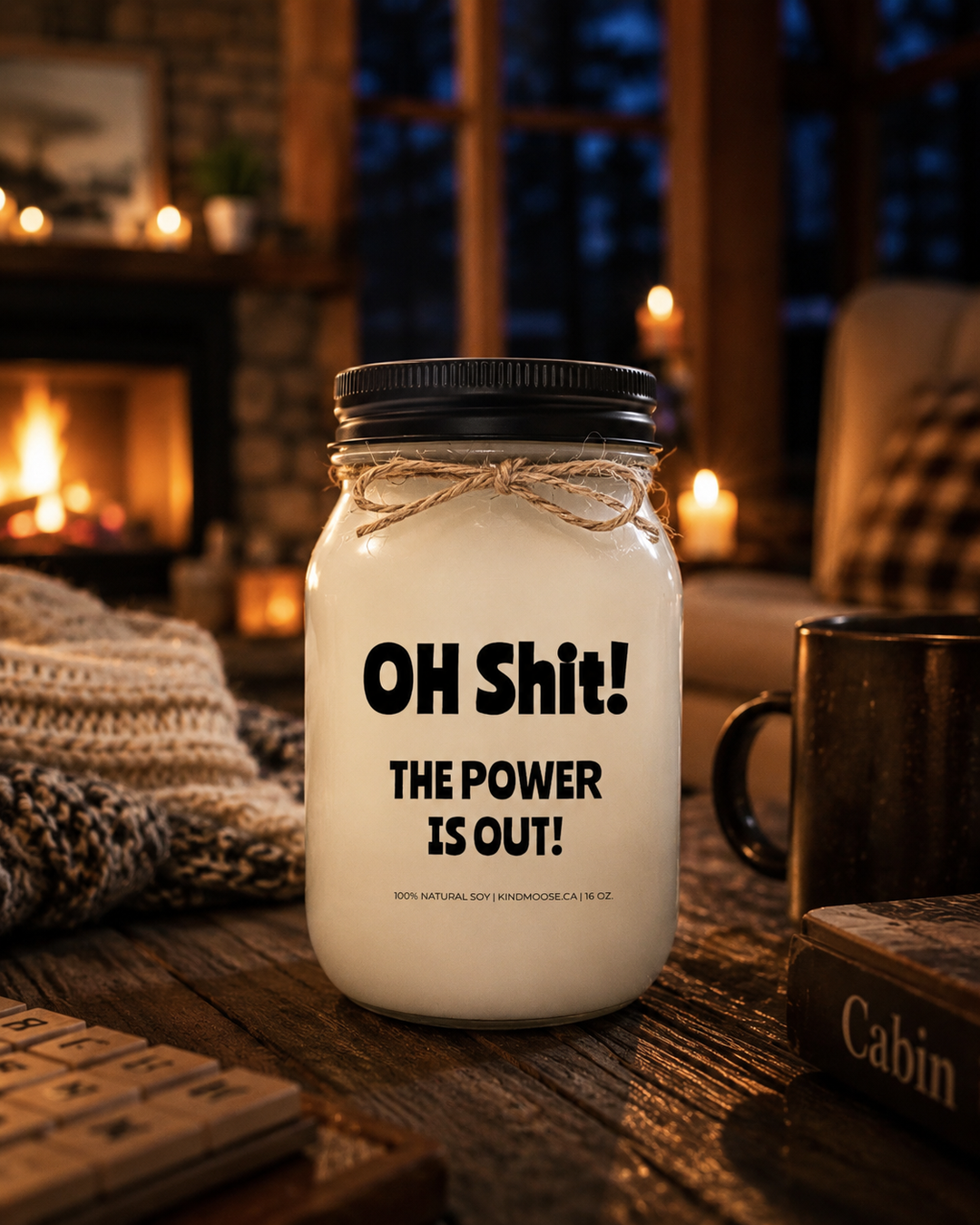 OH SHIT! THE POWER IS OUT! soy candle with black lid displayed on a rustic wood table inside a cozy Canadian cottage during a power outage, illuminated by warm candlelight and a glowing stone fireplace.