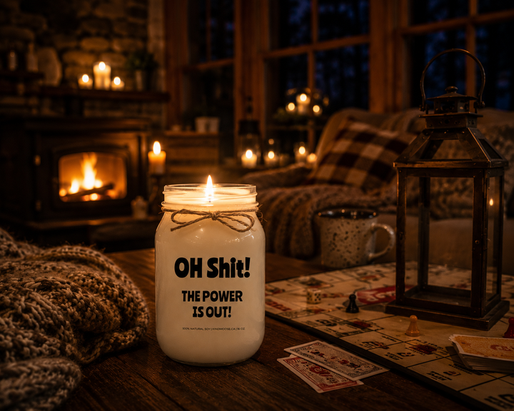 Burning OH SHIT! THE POWER IS OUT! soy candle inside a warm cottage featuring a stone fireplace, rustic wood furnishings, glowing candles, and a cozy power-outage atmosphere.