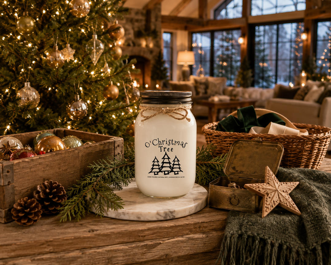 O' Christmas Tree customizable 16 oz soy candle with distressed bronze lid resting on a reclaimed white oak storage bench beside a beautifully decorated Fraser fir Christmas tree, surrounded by vintage ornaments, cedar branches, pinecones, and warm golden evening light in a luxury modern farmhouse.