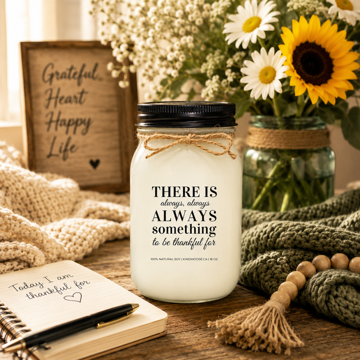 KINDMOOSE "There Is Always Something to Be Thankful For" inspirational soy candle beside a gratitude journal, fresh flowers, and cozy knit blankets in a warm farmhouse setting.