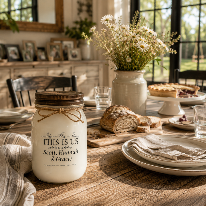 Personalized KINDMOOSE custom family candle with a distressed bronze lid displayed on a farmhouse dining table after a family meal, surrounded by artisan bread, linen napkins and warm afternoon sunlight, capturing togetherness and cherished family traditions.