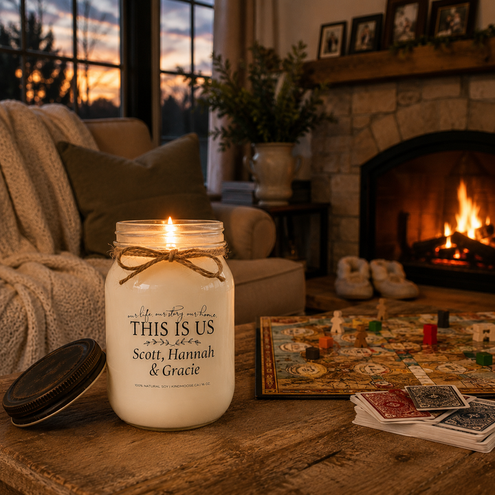 Burning personalized KINDMOOSE custom family candle with the distressed bronze lid resting beside it in a cozy modern farmhouse family room after game night, featuring a softly glowing fireplace, board game and warm evening atmosphere.