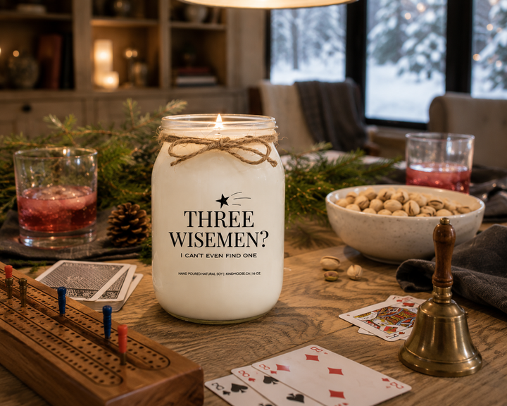 THREE WISE MEN? I CAN'T EVEN FIND ONE Christmas candle burning on a reclaimed white oak game table with playing cards, a cribbage board, cranberry mocktails, pistachios, and cedar greenery during a cozy farmhouse Christmas game night.